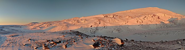 Montagne arrondie à peine éclairée de rose par le Soleil et couverte de neige.