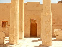 A large stone wall with a closed entrance and two rows of two columns preceding it