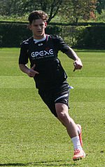 A young man wearing a black shirt and blackshorts, standing on a grass field