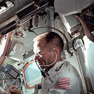 View from side of a white suited astronaught in an orbiting vessel writing with his right hand