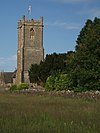 Stone three stage square tower surmounted by a flag pole. To the right are trees and in the foreground grass.