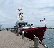 A Coast Guard corvette, in red, sits docked and flying Canadian naval ensigns