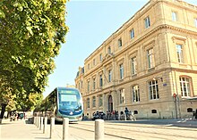 La faculté de droit, un bâtiment ancien. Un tramway passe devant, à côté de quelques arbres.