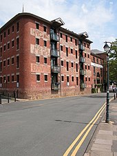 A red brick warehouse on four floors, now converted as flats. The loading doorways were slightly inset into the wall and now have protruding glazed balconies added.