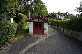 Vue d’un petit oratoire, maisonnette aux murs blancs et aux boiseries rouge sang.