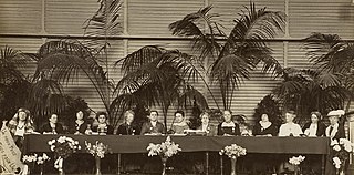 A black and white photograph of thirteen women delegates seated at a head table of a conference