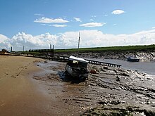 Muddy river bank with a small boat on it. Water can still be seen in the channel to the right.