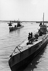 Black and white photograph of two World War II-era submarines on the surface of the sea. Land is visible in the background.