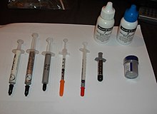 Several containers of thermal paste of different brands. From left to right: Arctic Cooling MX-2 and MX-3, Tuniq TX-3, Cool Laboratory Liquid Metal Pro, Shin-Etsu MicroSi G751, Arctic Silver 5, Powdered Diamond. In background: Arctic Silver thermal paste remover. Thermal greases.JPG