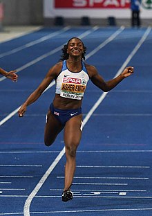 Dina Asher-Smith with a dark blue and white kit running on a blue track.