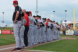 Men in mostly gray baseball uniforms lined up on baseball field's foul line