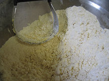 Butter and dry ingredients mixed together in a bowl. The result is not a uniform texture. The largest lumps are a bit bigger than the size of a pea.