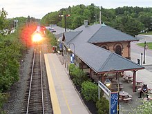 A modern passenger train arriving at an older stone railway station