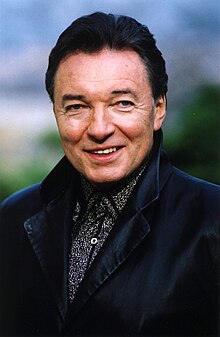 close-up of Karel Gott wearing a patterned shirt under a dark overcoat, smiling at camera