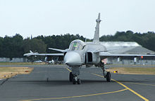 Jet aircraft taxiing against a background of a shed and green trees