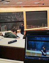 Foto de professor do Insper dentro da sala de aula com notebook aberto na transmissão da aula ao vivo para alunos que estão em casa.