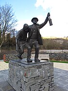 A memorial statue showing two men, a miner in difficulty, and a rescuer helping for half carry him. The statue if on a stone plinth.