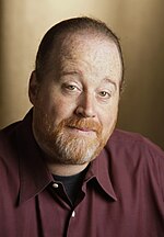 A picture of a bearded man wearing an unbuttoned maroon collared shirt.