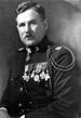 Head and torso of a man with neatly combed hair and a toothbrush mustache. He is wearing a dressy military uniform with an array of medals on his chest, a medal tightly around his neck, and shoulder cords.