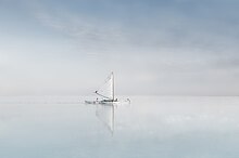 Une athmosphère cotoneuse, composée d'eau et de ciel, tout est calme et plat. Au centre, un petit bateau, avec son reflet estompé, une voile blanche pointée vers le ciel.