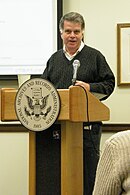 A gray haired man speaking in-front of a podium marked "National Archives and Records Administration 1985"