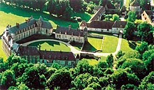 Photographie couleur aérienne d'un complexe d'élégants bâtiments de style « ferme provinciale », et de bois alentour.