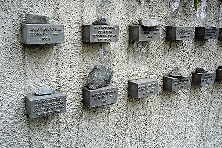 Namensblöcke an der Außenmauer mit darauf abgelegten Steinen