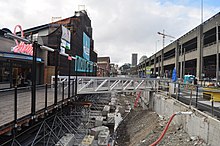 An open trench with a temporary steel bridge separates a boardwalk business from a parking lot.