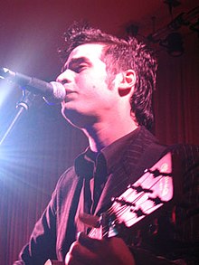 Young curly-haired male singing or speaking into microphone.