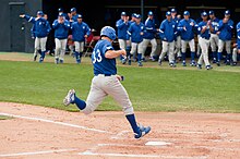 A Highlanders baserunner scores a run as teammates emerge from the dugout to greet him during a 2011 baseball game Justin Shults (5478337118).jpg