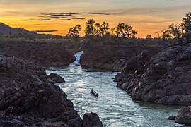 Li Phi falls at sunset with orange sky and a fishing boat in Don Khon Si Phan Don Laos