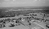 Gammelt flyfoto av Nøtterøy kirke i jordbrukslandskap og villabebyggelse langs fylkesvei 308 ved Borgheim på øya Nøtterøy Foto: Widerøe/Vestfoldmuseene