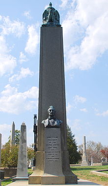 Photographie d'un obélisque gris situé dans un cimetière derrière un buste de Tyler.
