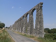 Vue des vestiges d'un aqueduc antique longeant une route.