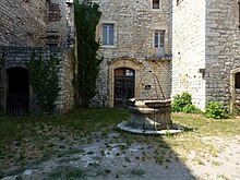 Coin d'une cour herbeuse, entourée d'un bâtiment de pierres. Le puits au centre est cerclé de fer.