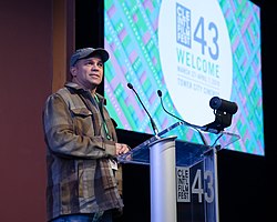 a man stands at a podium, with the film festival logo projected on a screen behind him