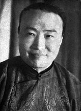 A black-and-white image of a jovial-looking man looking forward. His shirt has ornate patterns on it.