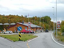 Foto eines Grenzübergangs mit Zollschildern und einigen Autos. Im Hintergrund ein Wachturm