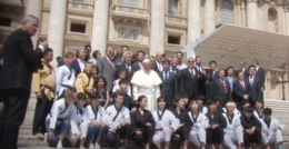 A group of taekwondo athletes, suited men, and Pope Francis on some stairs