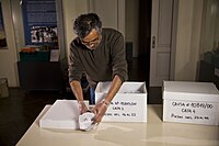 Man shown handling artifacts wrapped in white material on a table. There are two boxes with artifacts in them.