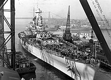 A large warship in the final stages of completion; the main and secondary guns have been fitted, but the deck is cluttered with various materials presumably used in building the ship