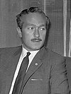 Colin Chapman in a black and white photograph sporting a mustache and looking to the left of the camera