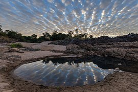 Water reflection of stringy gray and white clouds in a pond on a sand beach of Don Khon at sunrise in Laos