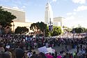 Demonstrators fill streets, sidewalks, and plazas on a sunny day. A tall, white building stands in the background.