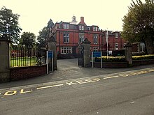 some large gates, with a red brick building with cupola beyond