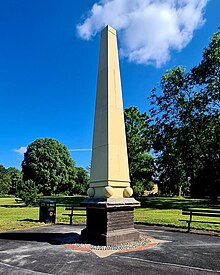 A pale stone obelisk stood on a dark brick base in lawns