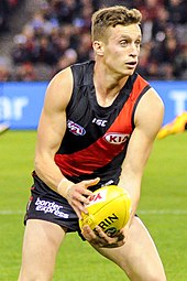 Male athlete in sleeveless guernsey holds football