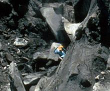 A man climbing a steep cliff face dwarfed by massive boulders around him.