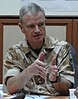 A seated, grey-haired man in desert camouflage uniform