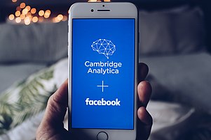 A white iPhone with the illustration Facebook + Cambridge Analytica